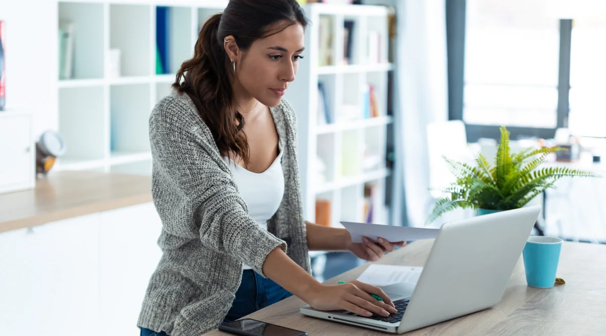 Woman handling papers and using laptop