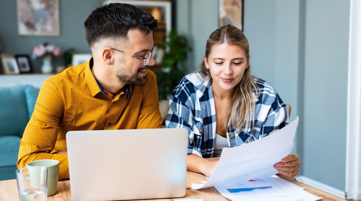A married couple sits together in their living room and reviews a document