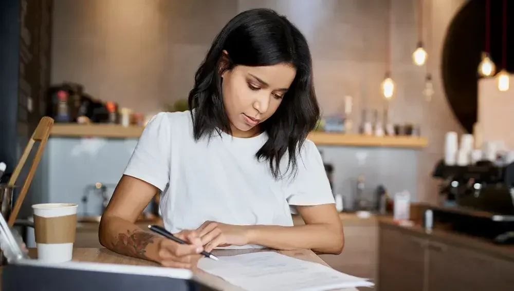 An inventor sits at a counter in her shop and fills out paperwork for a new patent.