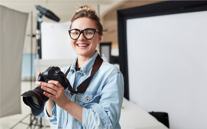 An image of a photographer smiling and holding the camera in a studio. 