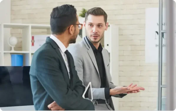 Man wearing a grey suit with a black shirt talking to a male coworker in a black suit with white shirt and black tie discussing doing their business dissolution with LegalZoom.