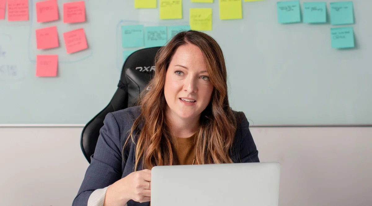 Woman speaking, with notes on a whiteboard