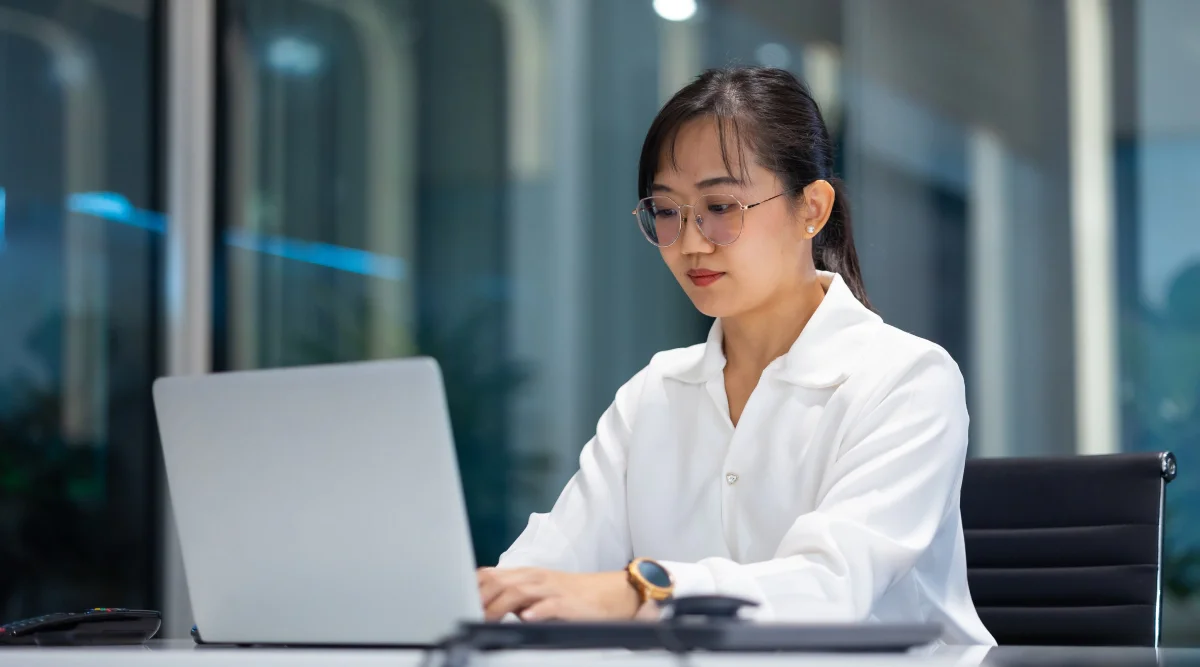 Woman in white blouse focused on laptop in office