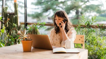 Woman on a phone call working on a laptop outdoors