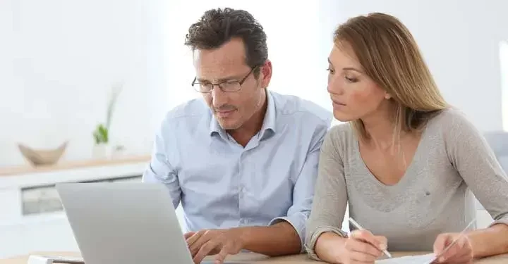 A young couple sits close together, looking at a laptop screen as they discuss what happens if a domestic partner dies without a will.
