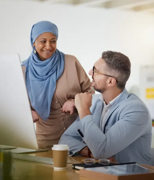 A woman in a blue hijab stands and speaks with a man wearing a business suit and glasses.