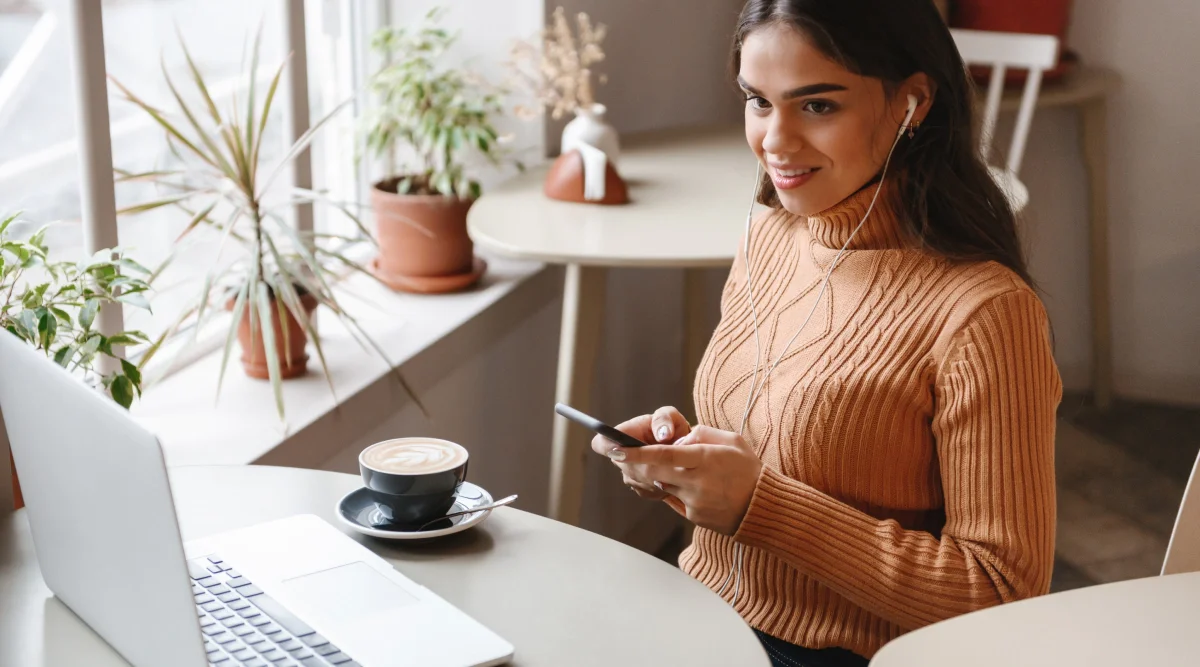 Woman with earbuds holding phone at a cafe