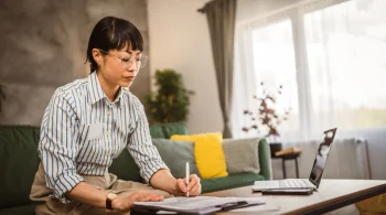 Woman writing notes, laptop on table