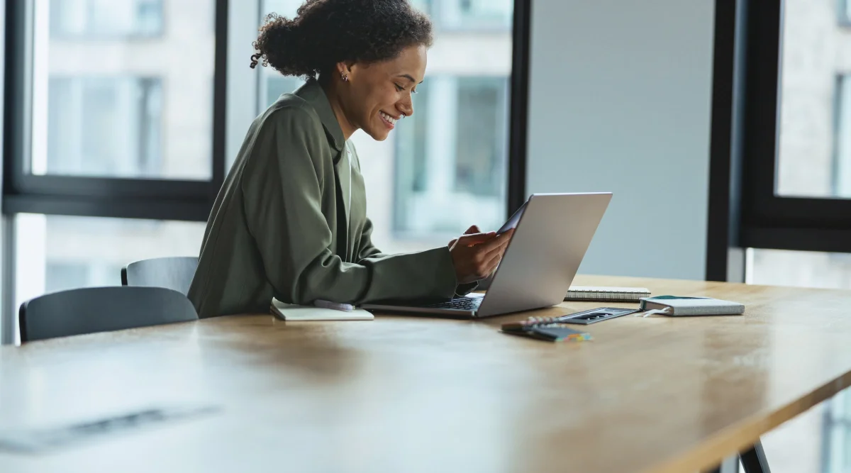 Smiling woman in green shirt using a laptop at a large desk