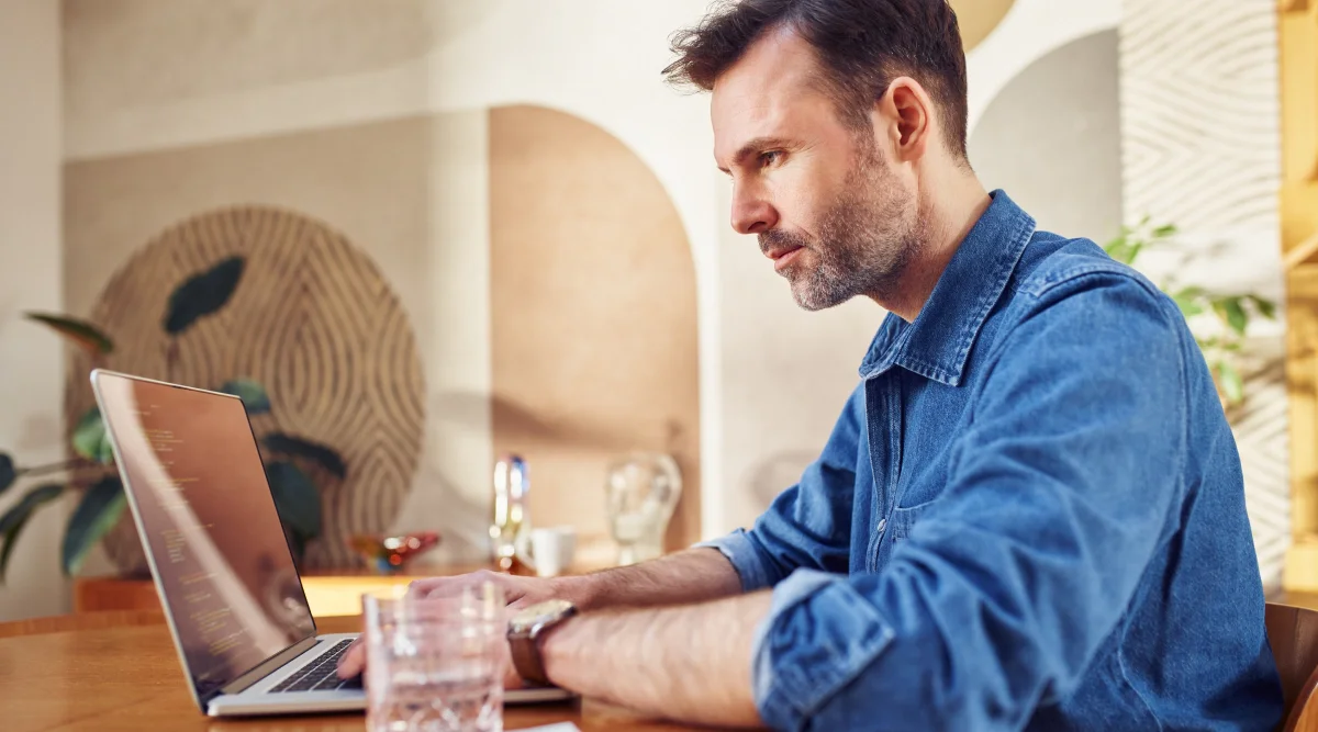 Man in denim shirt focused on a laptop at home