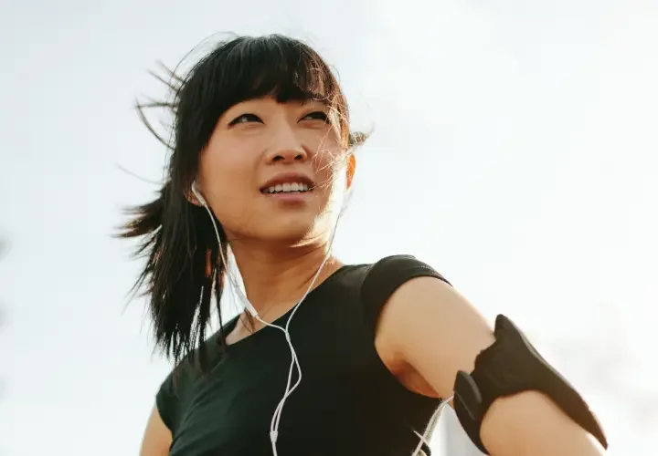 An asian woman looks onto the horizon in workout gear while listening to headphones.