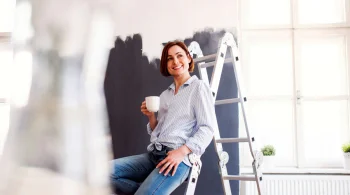 Woman with a cup, sitting on a ladder in a bright room