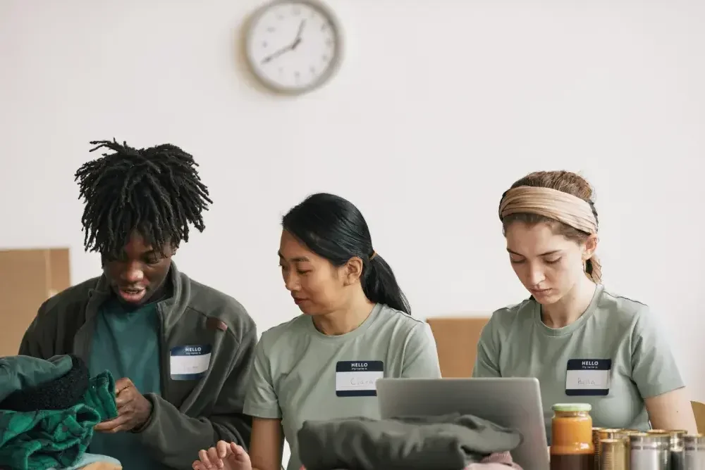 Three volunteers from a charitable organization sit at a table and work on a project together. If they apply for nonprofit status, that may help their credibility in the community.