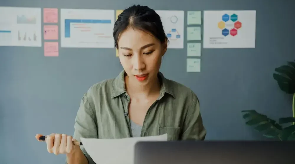 A woman sits at a desk reading over a piece of paper.