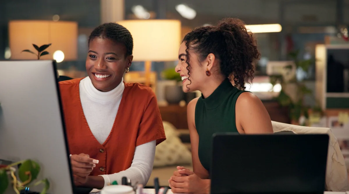 Two women laughing and working on a computer