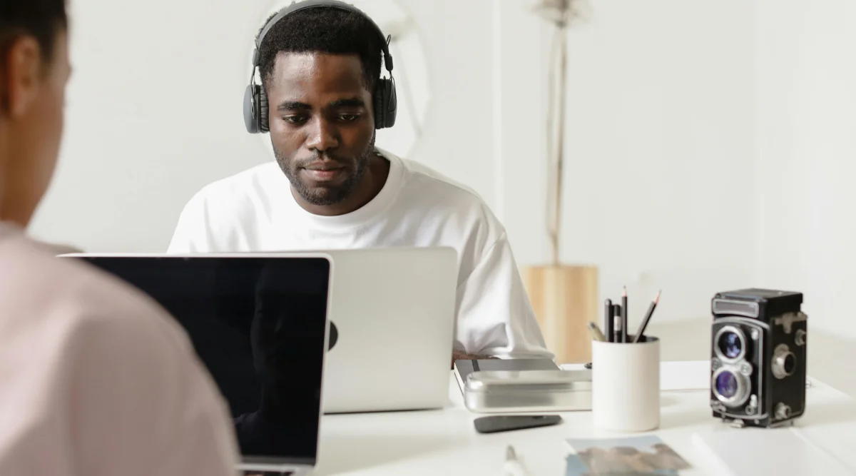 A man wearing headphones sits at a conference table and uses his laptop.