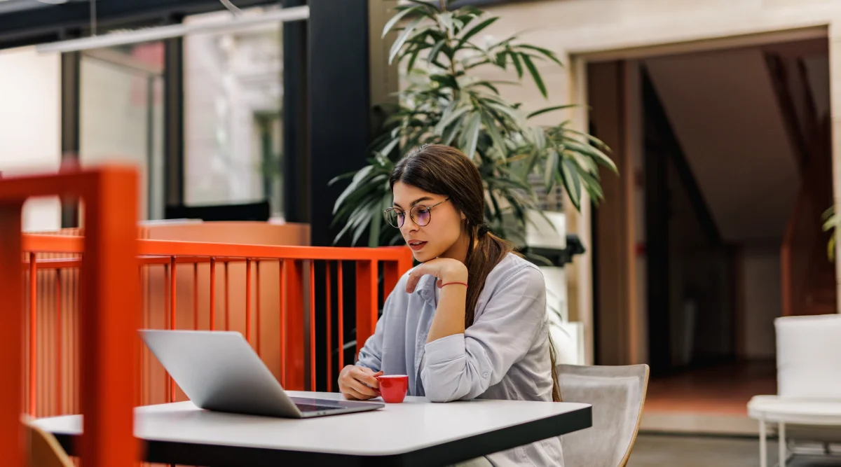 Woman with red cup working on a laptop in a cafe