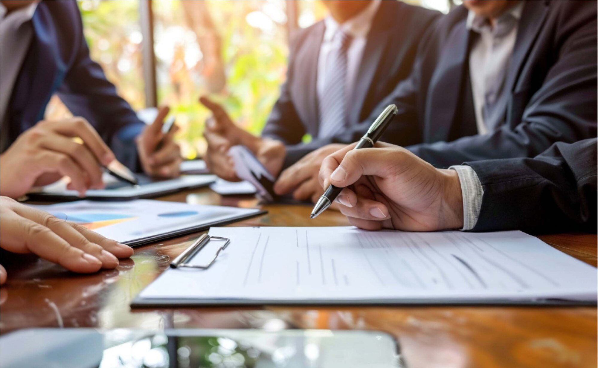 An image of 4 people discussing in a meeting room and 1 of them signing an agreement.