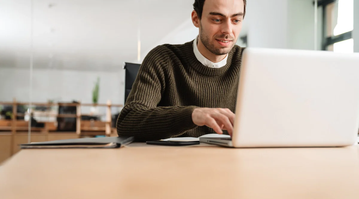 Man in sweater smiling while typing on laptop