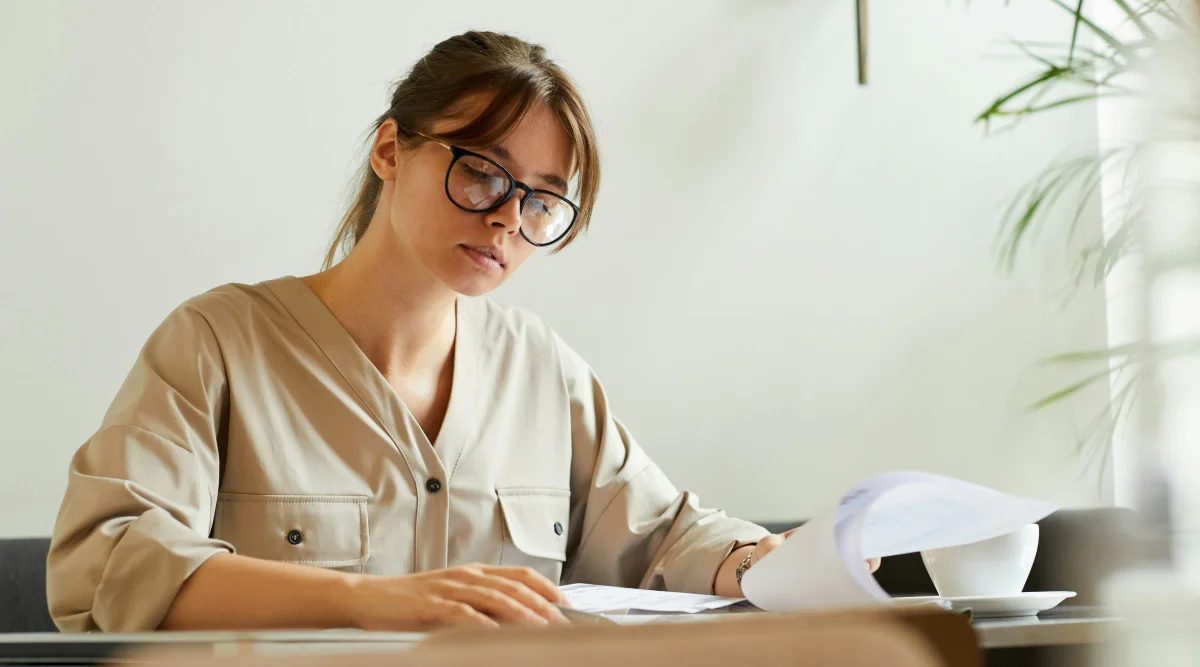 A woman sits at her desk flipping through documents.