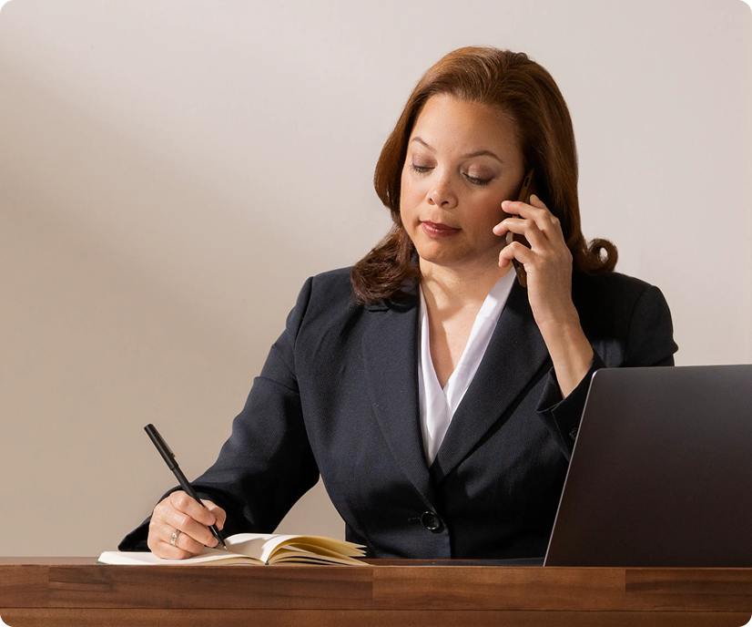 woman sitting at her desk making a call and taking notes.