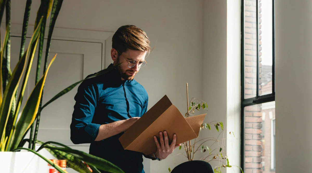 Man reading documents by a window with plants