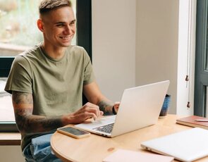 A man with tattoos laughing while chatting with a coworker at a desk