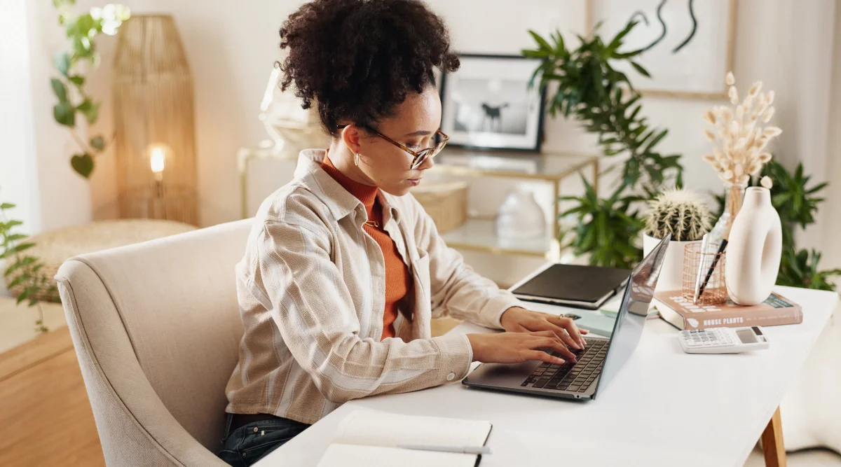 Woman in a cozy room typing on a laptop at a desk