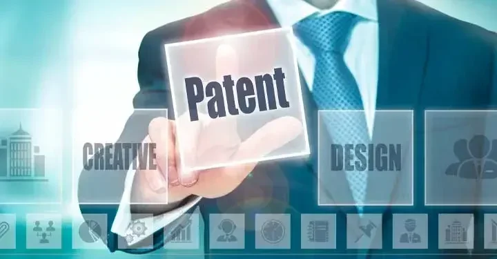 A person in a suit and tie touches the "Patent" button on a screen with other icons and words.