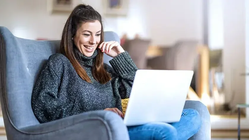 A woman sitting in a comfy chair smiles as she reads online about how to form an LLC in Washington, D.C.