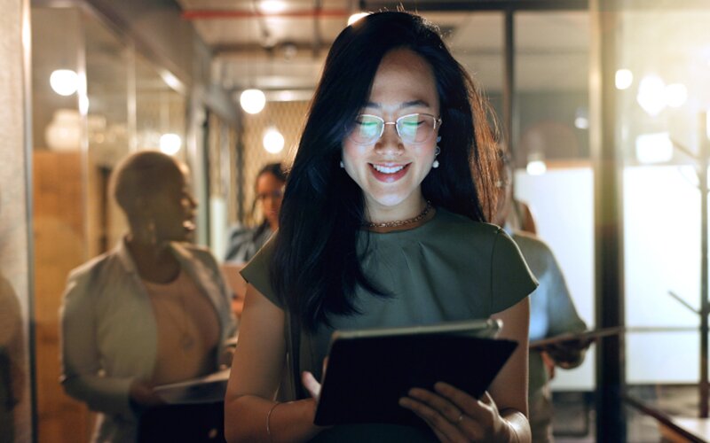 An image of a lady smiling and looking at a tab inside an office.