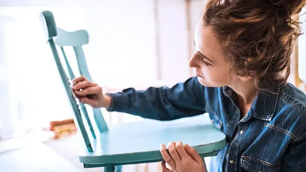A woman refinishes a chair in her shop as she ponders her DBA name.