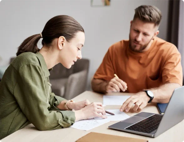 Brunette white woman with her hair in a pony tail wearing a long sleeved green blouse sitting next to a brunette White man wearing a orange shirt sitting in front of a laptop discussing their LegalZoom business dissolution.