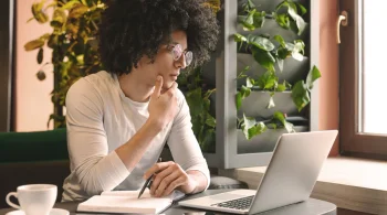 Man in glasses thinking while working on a laptop