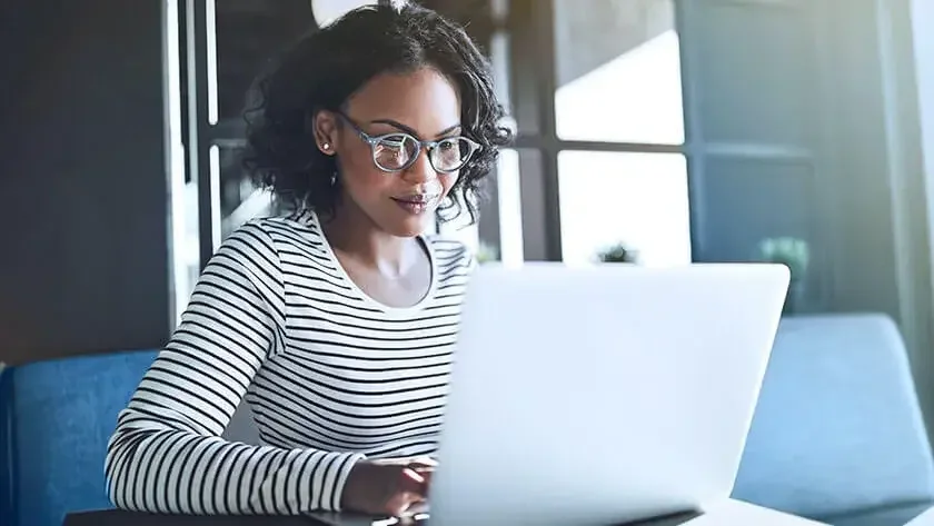 A woman in a striped long-sleeve top sits at a conference table on her laptop.
