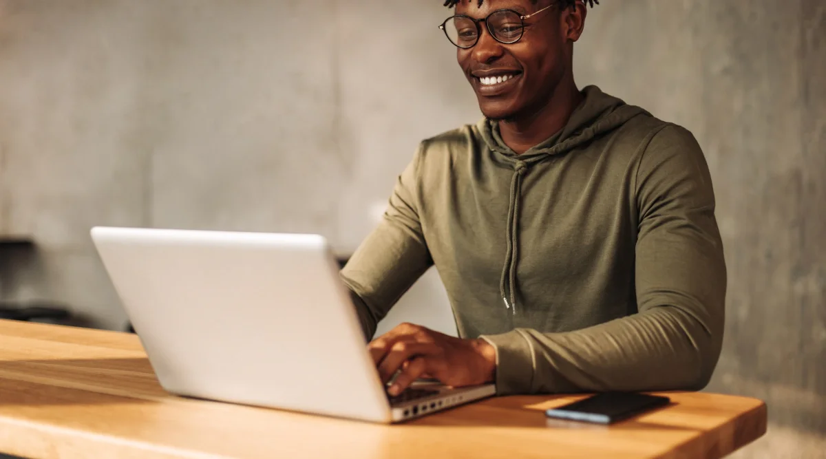 Smiling man in hoodie using laptop at a table