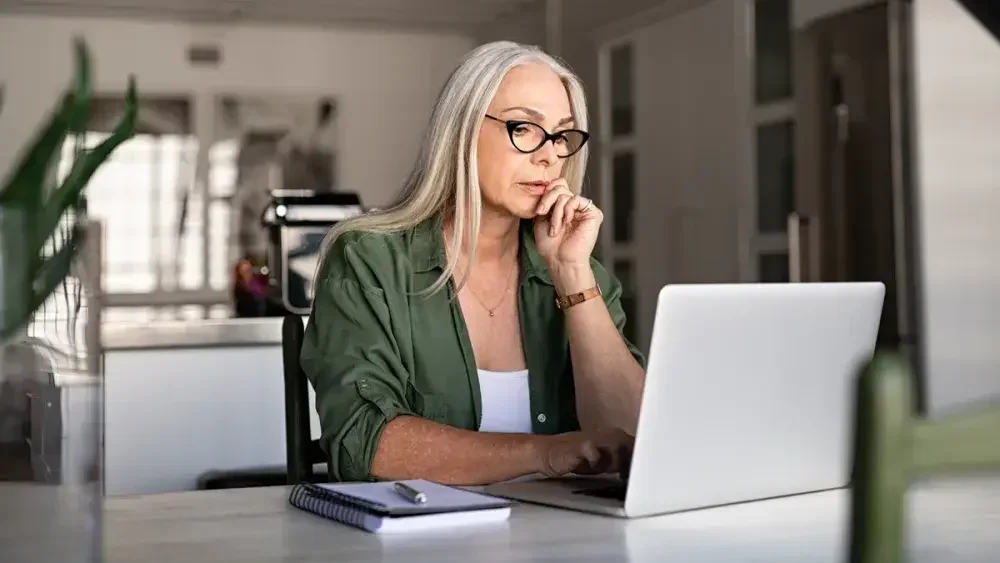 A woman seated at a table fills out a last will and testament template on her laptop. Using such a template allows you to write a legally valid will without the fees associated with hiring an attorney.