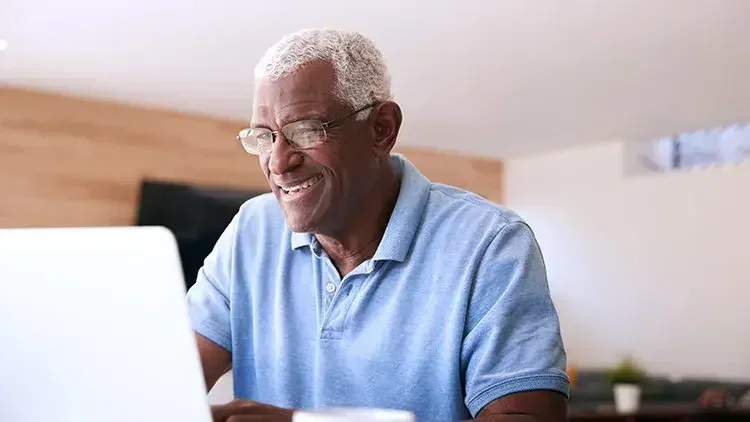 Senior man looks at laptop smiling.