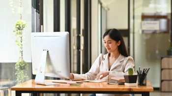 Woman writing notes at a computer desk