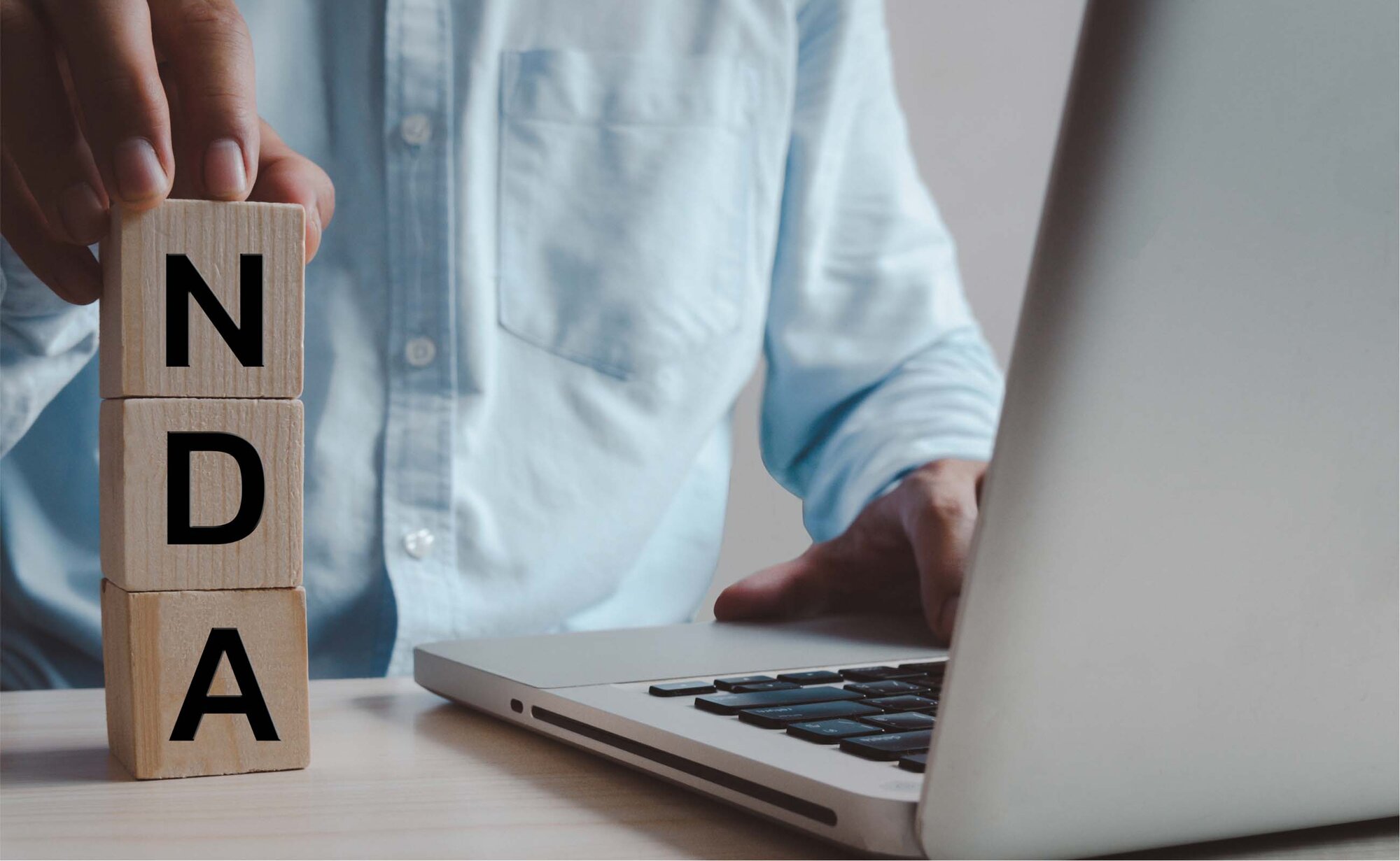 An image of an employee holding NDA wooden blocks and sitting in front of a laptop.