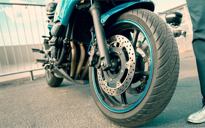 An image of a person standing next to a motorcycle's tire.