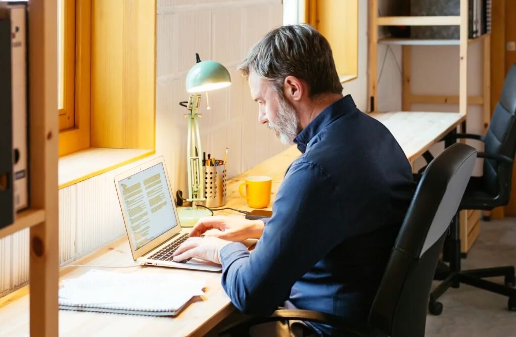 A man sits in his well-lit office and uses a laptop