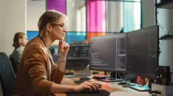 Woman coding at a dual-monitor setup in an office