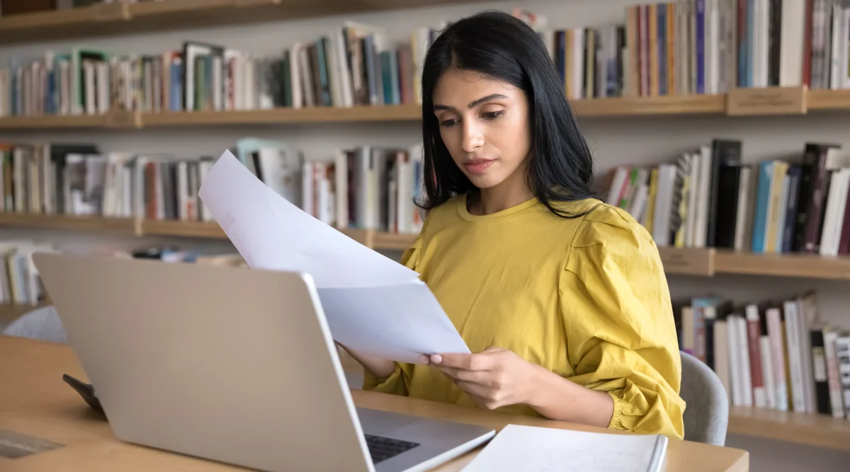 Woman in yellow reading papers in a library setting