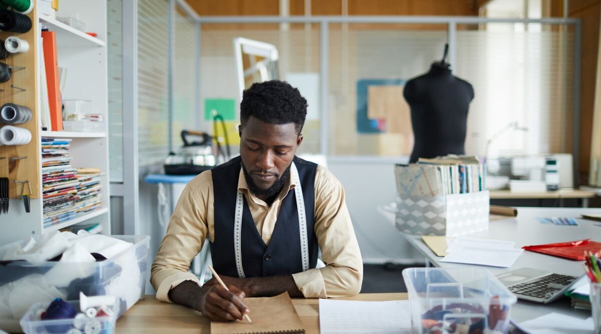 A tailor works in his shop and draws a picture of his latest sewing machine invention that he hopes to patent.