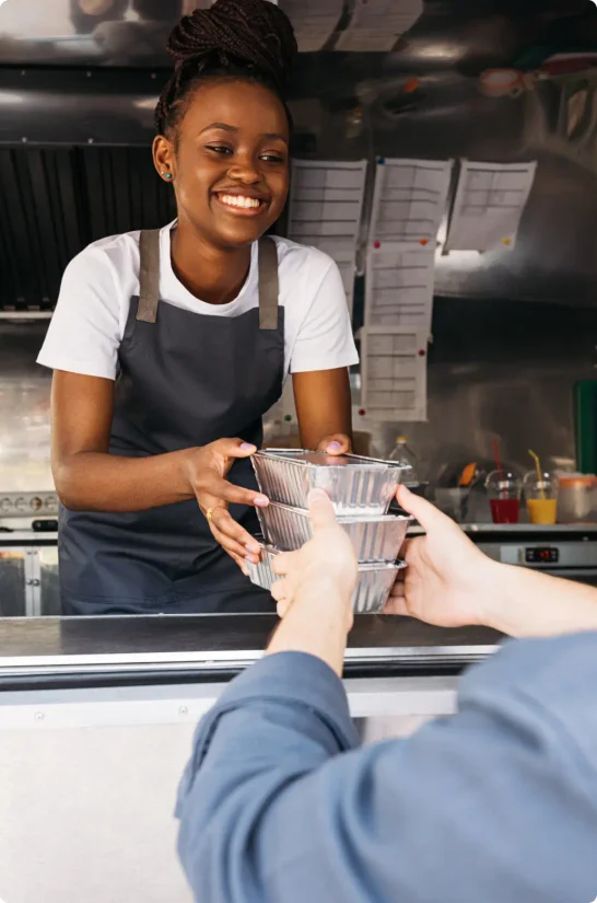 a young woman works the counter of a food truck and hands an order to a customer.