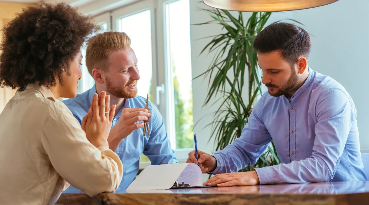  A couple sits across from an attorney in a modern, bright office, reviewing estate planning documents on a wooden desk.