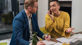 Woman on phone, discussing with a colleague at a desk