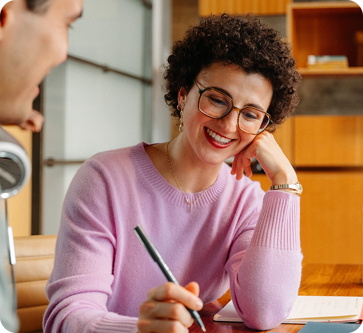 Woman with curly hair and pink shirt takes notes on how to improve their business 