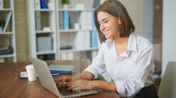 Woman smiling while typing on a laptop in an office